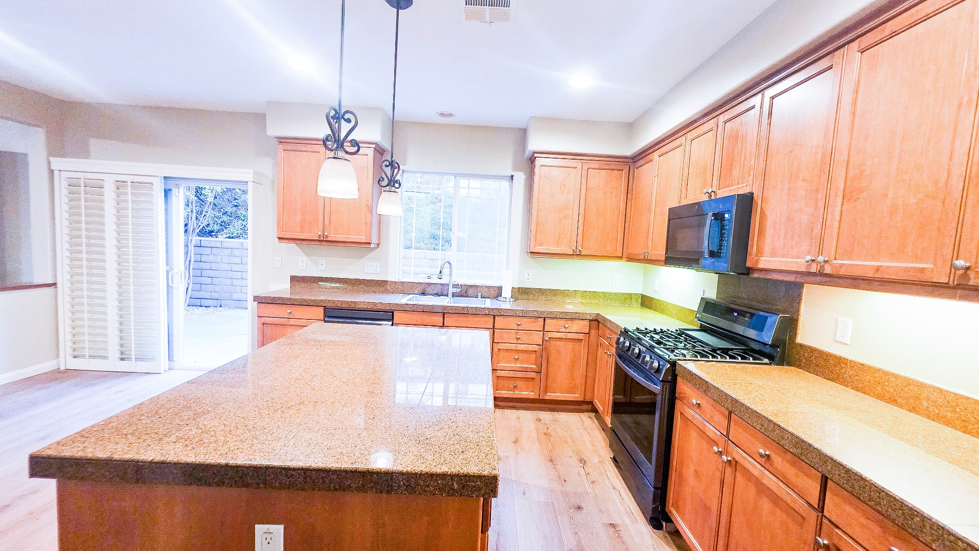 Bright kitchen with large island, gas range, wood cabinets and slider to backyard